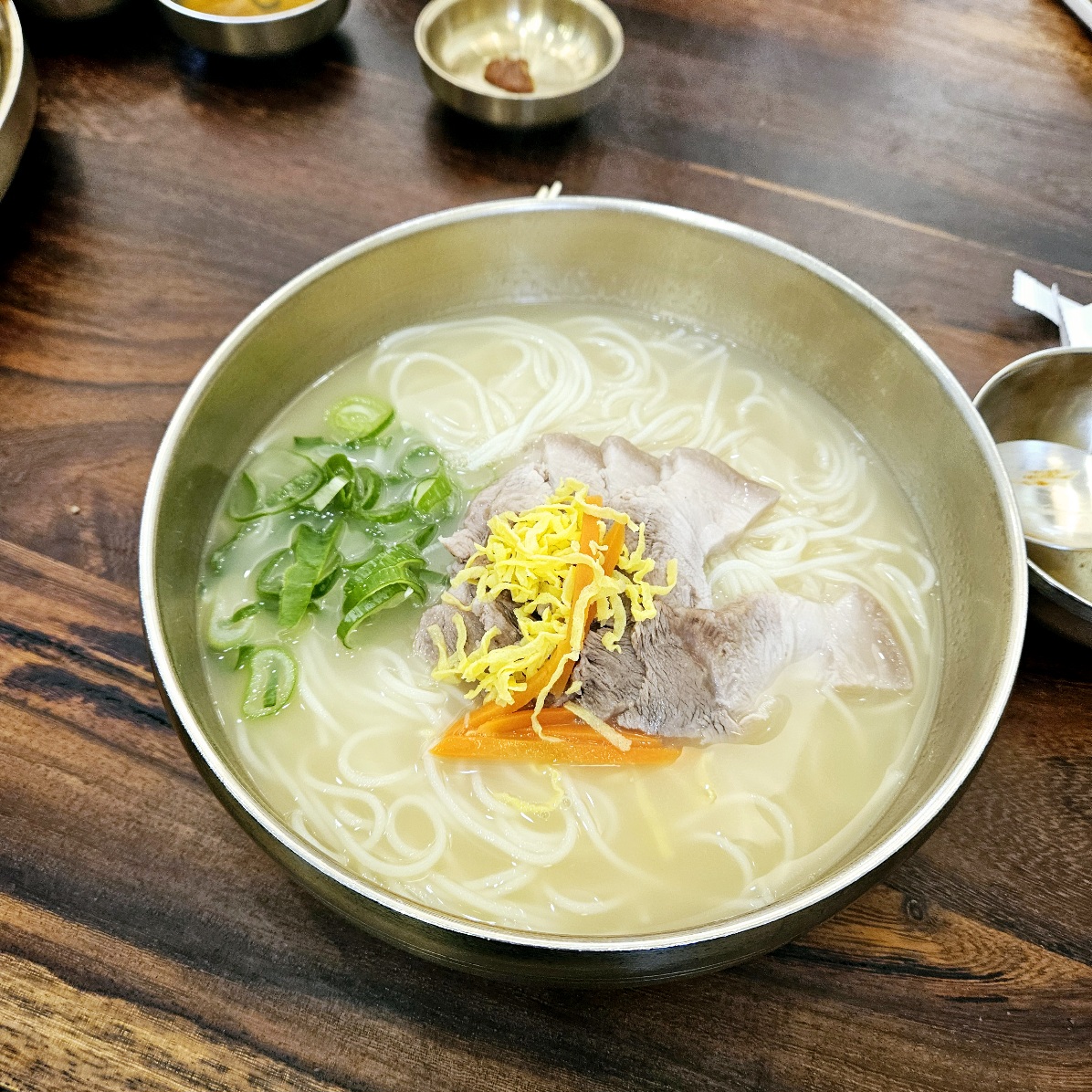 제주 먹돌 본점의 고기국수. 깊고 담백한 사골 육수에 쫄깃한 면발, 그리고 부드러운 돼지고기 고명이 올라가 있다. 대파와 계란 지단, 채 썬 당근이 더해져 색감까지 조화를 이루는 한 그릇.
