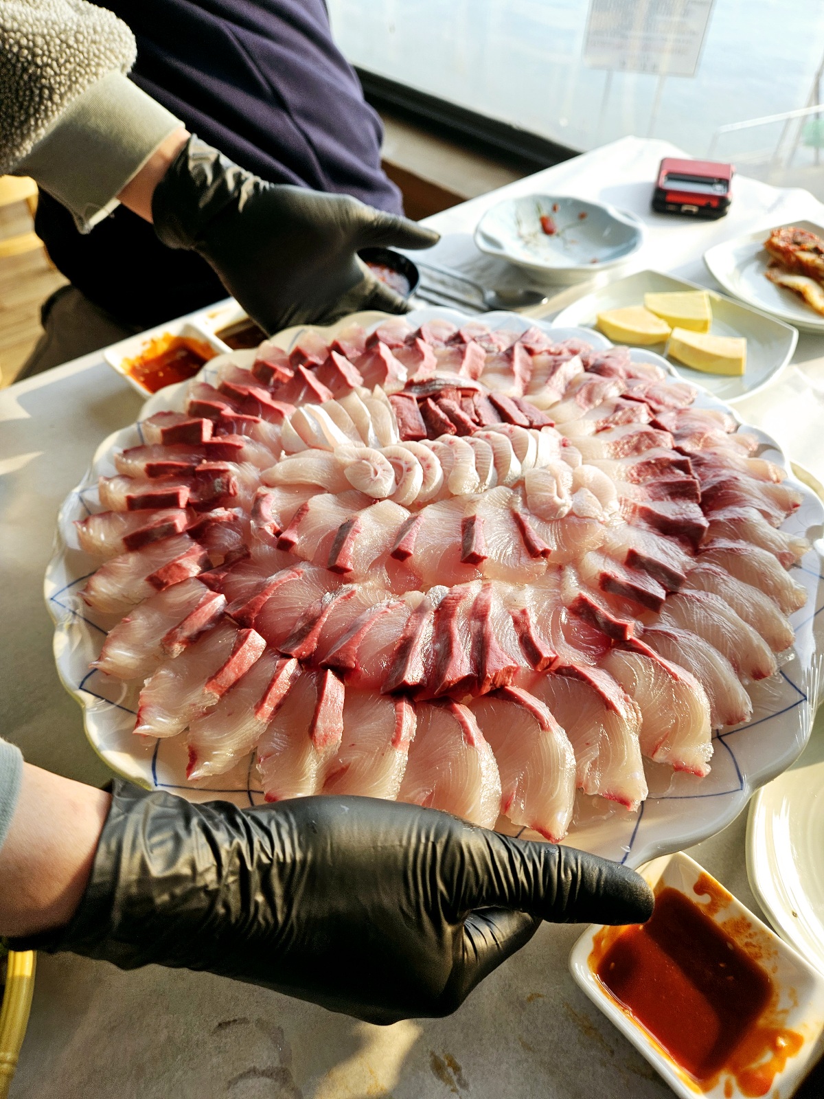 당진 한진포구 횟집 현대회센터에서 방어회, 멍게, 낙지 등 다양한 해산물 요리와 함께 탁 트인 바다 전망을 즐기는 모습. 방어철 제철 회의 비주얼과 함께 푸짐한 기본찬이 인상적인 현장 분위기