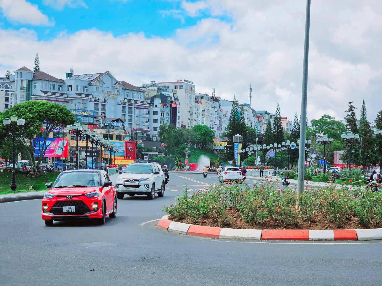 달랏 카페! 달랏 시내 중심 거리의 활기찬 모습. 오토바이와 차량이 오가는 도로 옆으로 쑤엉흐엉 호수와 상점들이 줄지어 있다. 하늘은 맑고 파란 날씨다.