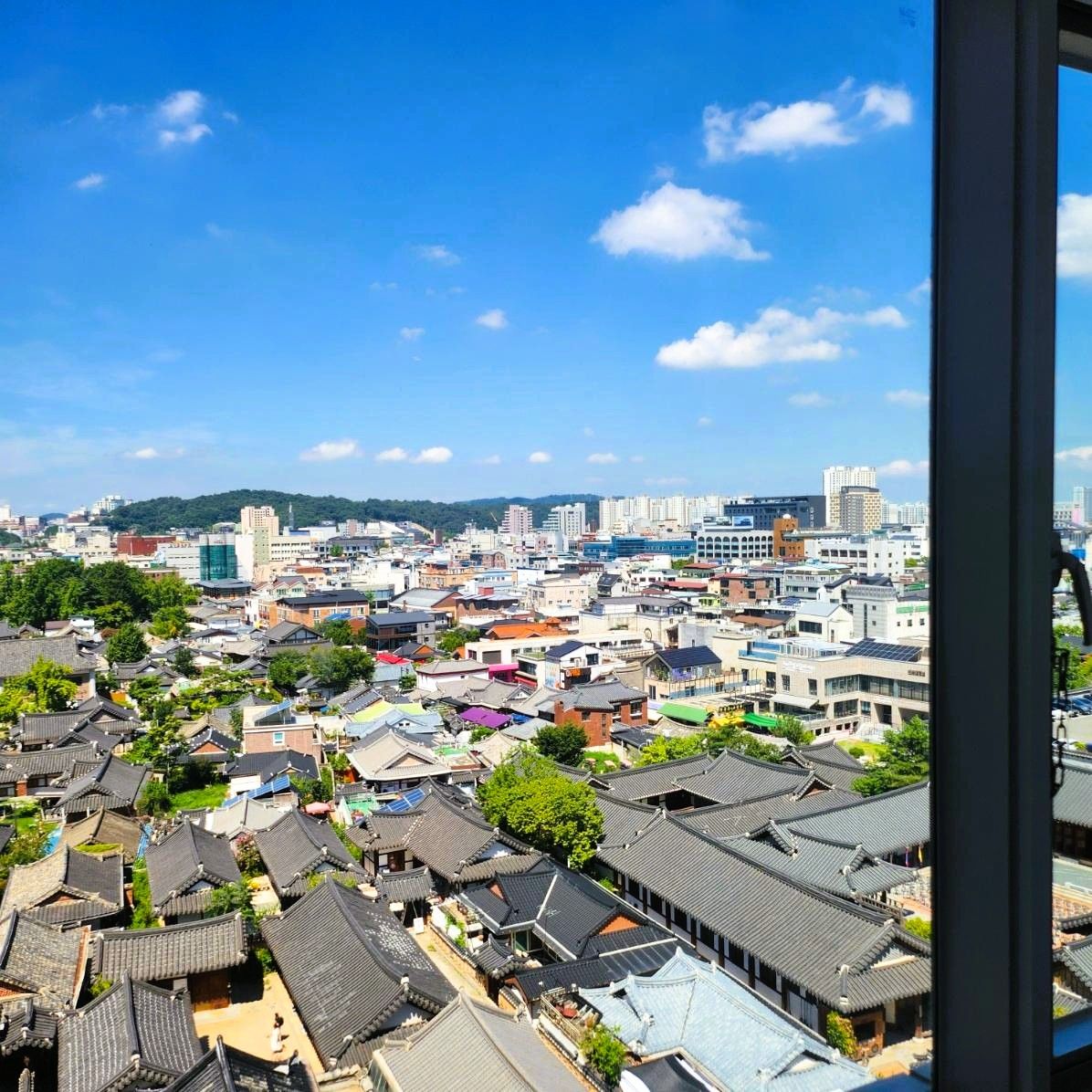 전주 라한호텔 객실에서 바라본 한옥마을과 전주시 도심의 낮 전경. 푸른 하늘과 고즈넉한 한옥 지붕이 대비되는 풍경
